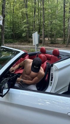 a shirtless man sitting in the driver's seat of a white convertible car