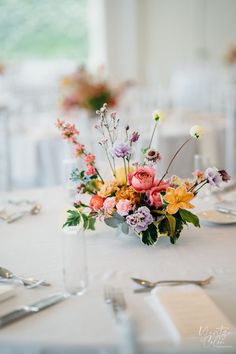 an arrangement of flowers on a table in a room with white linens and silverware