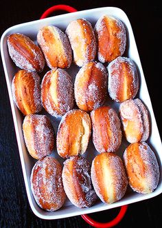 powdered sugar covered doughnuts in a white dish on a black table top