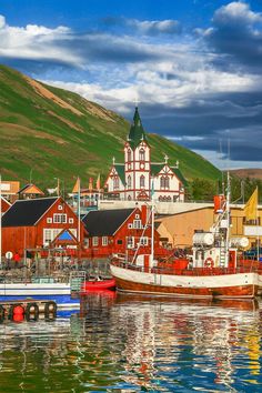 several boats are docked in the water near some red buildings and green hills behind them