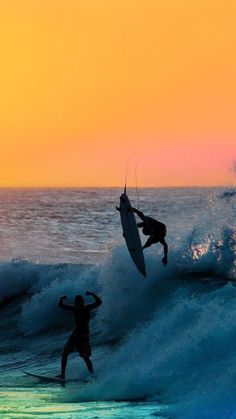 two surfers are riding the waves in the ocean at sunset, one is jumping off his surfboard