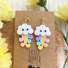 a pair of earrings with clouds and rainbows hanging from them on top of a piece of paper