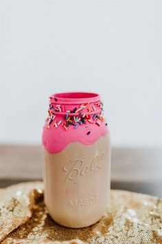 a pink mason jar with sprinkles on it sitting on top of a table