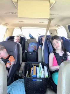 two children in the back seat of a car with books and toys inside it, while another child sleeps