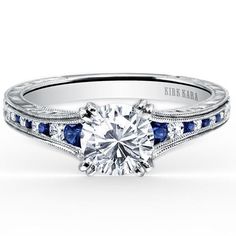 a white gold engagement ring with blue sapphires on the sides and an engraved band