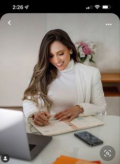 a woman sitting at a table with a notebook and cell phone in front of her