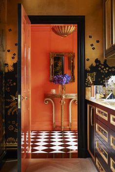 an orange bathroom with black and white checkerboard flooring, gold framed mirror and vanity