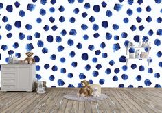 a teddy bear sitting on top of a rug in front of a wall with blue polka dots