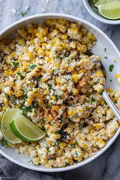 a white bowl filled with corn and topped with a lime wedge next to a spoon