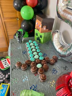 a table topped with lots of cupcakes next to a bunch of foil balloons