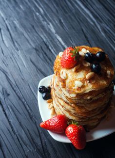 a stack of pancakes topped with fruit and nuts on a plate next to two strawberries