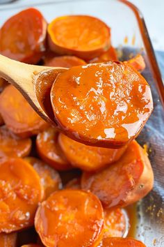 a wooden spoon full of cooked carrots on top of a glass dish with sauce