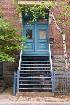 a blue door is on the side of a brick building with stairs leading up to it