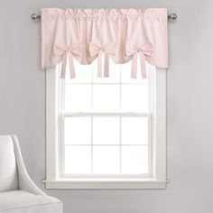 a white chair sitting in front of a window with pink bow valances on it