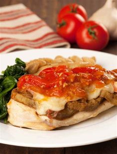 a white plate topped with lasagna covered in sauce next to spinach and tomatoes