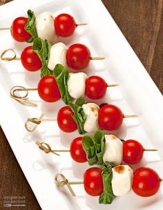 tomatoes and mozzarella skewers are arranged on a white plate