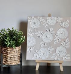 an easel next to a potted plant on top of a wooden table with white paper flowers