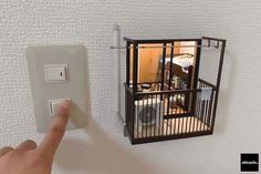 a hand is pointing at an electrical outlet with a cage on the wall above it