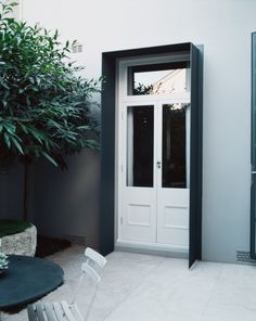 a white door is open in front of a table with chairs and a potted tree