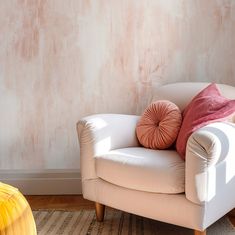 a white chair sitting in front of a wall with a pink pillow on top of it