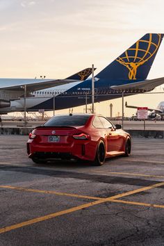 a red sports car parked in front of an airplane on the tarmac at an airport