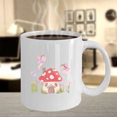 a white coffee mug with a mushroom house and fairy on the side, sitting on a table