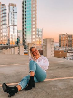 a woman sitting on the ground in front of some tall buildings with her legs crossed