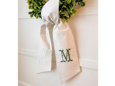 a white towel with the letter m on it hanging from a wall next to a plant