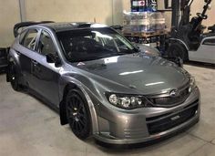 a silver subarunt parked in a garage next to other cars and equipment on the floor