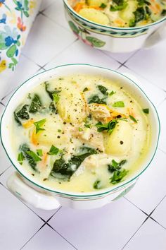 two bowls filled with soup on top of a tiled counter next to a spoon and napkin