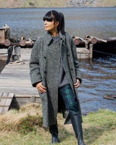 a woman standing on top of a grass covered field next to a body of water