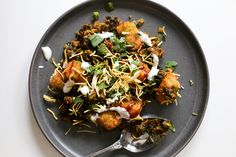 a black plate topped with food on top of a white table next to a silver spoon