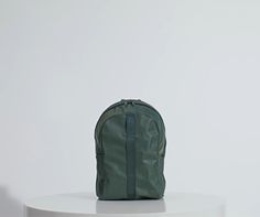 a green backpack sitting on top of a white table in front of a white wall