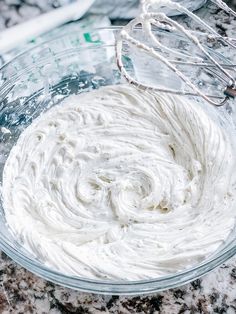 a bowl filled with whipped cream sitting on top of a counter next to a whisk