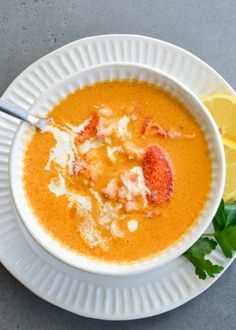 a white bowl filled with soup and garnished with lobster on the side next to a lemon wedge