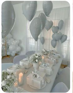 the table is decorated with white and silver balloons, gift boxes, candles, and flowers