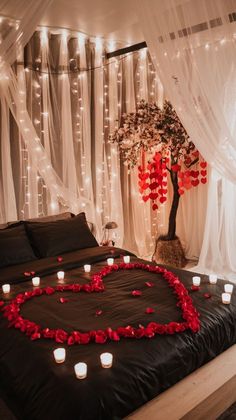 a bed topped with lots of red roses next to a tree filled with white lights