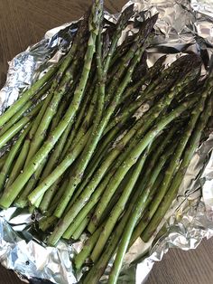 asparagus spears on aluminum foil sitting on top of a wooden table, ready to be cooked