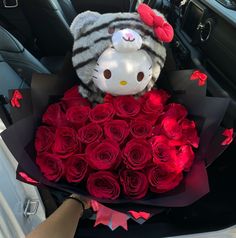 a hello kitty stuffed animal sitting in the back seat of a car with red roses