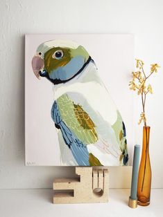 a colorful bird sitting on top of a wooden block next to a vase with flowers