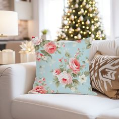 a living room with a christmas tree and flowers on the pillow cover, in front of a white couch