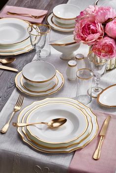 the table is set with white and gold plates, silverware, and pink flowers