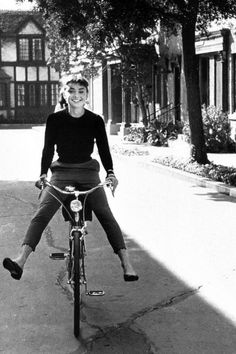 a man riding a bike down a sidewalk next to a tree and building in the background