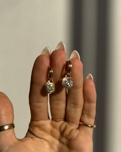 a woman's hand holding two gold rings with diamond stones on each one and the other