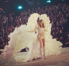 a woman in a white feathered outfit walking down a runway