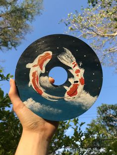 a hand holding up a disc with koi fish painted on it