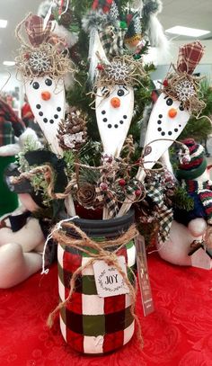 some snowmen are sitting next to a christmas tree in a mason jar on a red table cloth