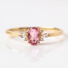 an oval shaped pink sapphire and diamond ring with two white diamonds on the band, set in yellow gold