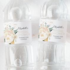 two clear water bottles with white flowers on the top and one is labeled bridal shower