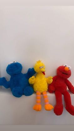 three stuffed animals sitting next to each other on a white surface and one is red, the other blue